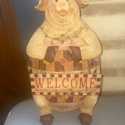 Sale Photo Thumbnail #239: Decorative standing pig statue made of carved-look painted resin, featuring a checkered pattern, floral details, and holding a hanging 'WELCOME' sign on small metal chains. Country style decor suitable for tabletop, entryway, or porch display. In good pre