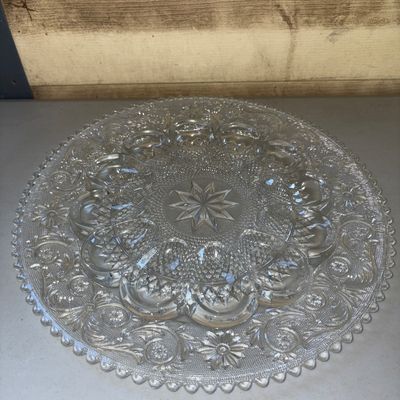 Sale Photo Thumbnail #208: Clear pressed glass deviled egg serving tray or platter featuring an intricate starburst and floral scroll pattern with egg-shaped indentations around the ring. Good condition with no visible chips or cracks.
12in