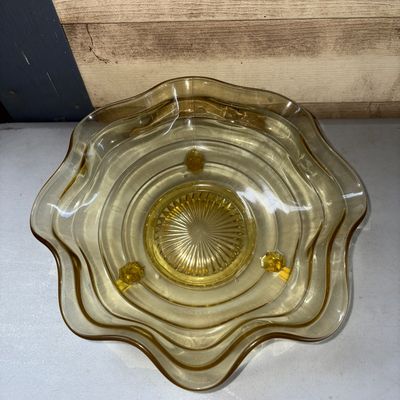 Sale Photo Thumbnail #311: Vintage yellow amber glass bowl featuring a crimped/ruffled edge and three small feet. The center base exhibits a molded starburst/sunburst pattern. Appears to be in good condition with no visible chips or cracks.
10in