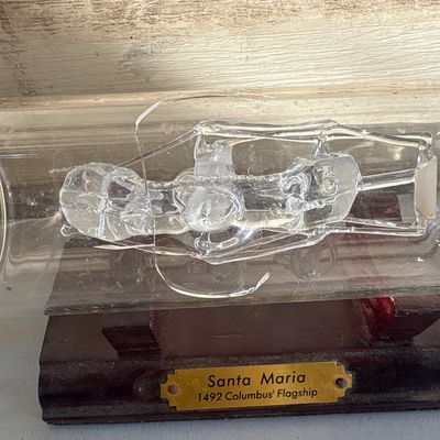 Sale Photo Thumbnail #347: Collection of three glass decorative items including a hand-blown glass ship in a bottle mounted on a wooden base labeled 'Santa Maria 1492 Columbus' Flagship' (note: glass rigging inside bottle appears broken/detached), alongside two laser-etched crystal