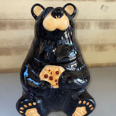 Sale Photo Thumbnail #168: Glazed ceramic cookie jar shaped like a sitting black bear holding a chocolate chip cookie. Removable head lid. Appears to be in good condition with no visible cracks or chips.
12in tall