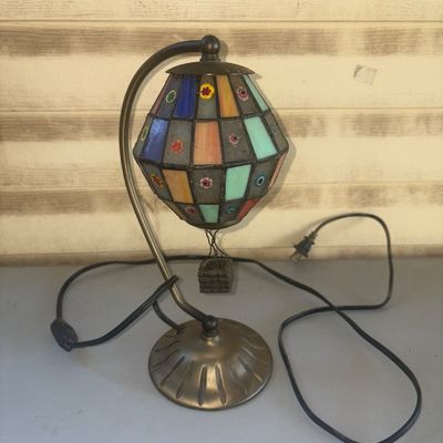 Sale Photo Thumbnail #244: Unique stained glass accent lamp designed in the shape of a hot air balloon with a small suspended basket. Features multicolored leaded glass panels inset with floral millefiori glass accents. Bronze-tone metal gooseneck arm and base. Includes attached po