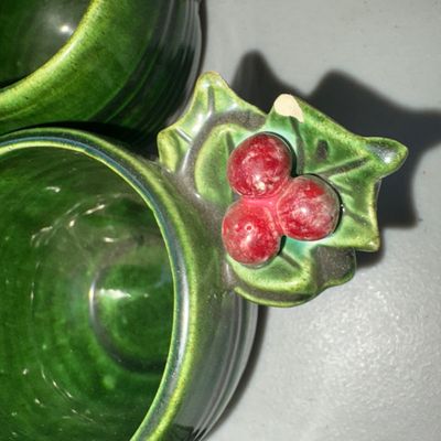 Sale Photo Thumbnail #339: A ceramic holiday punch bowl set featuring a green glazed finish with raised holly leaf and red berry accents around the rims and handles. Includes 1 large punch bowl, 1 ceramic ladle, and 12 matching cups. Minor wear visible, including a small chip on on