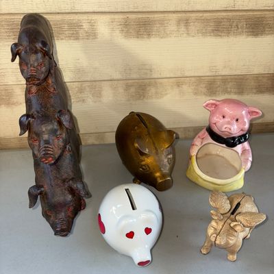 Sale Photo Thumbnail #63: Collection of five pig-themed items including a dark resin or cast stacked pig figurine, brass/metal pig bank, a winged cast metal pig bank, a ceramic pink pig planter/holder, and a ceramic white pig bank with red hearts. Items show light surface wear con