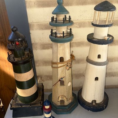 Sale Photo Thumbnail #276: Set of four decorative wooden lighthouse figurines in various sizes and nautical styles. Features painted finishes, rope accents, netting details, and crackle paint effects. Items show light surface wear consistent with age and display. The top cap on one
