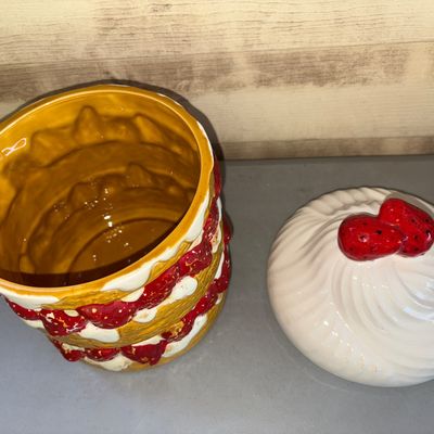Sale Photo Thumbnail #177: Ceramic cookie jar shaped like a layered strawberry shortcake with a whipped cream lid topped with strawberries. Shows some light surface paint wear and minor distress to the painted detail, typical for vintage ceramics, but overall in good usable conditi