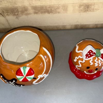 Sale Photo Thumbnail #183: Glazed ceramic gingerbread girl cookie jar featuring festive holiday details including a red polka dot bow, peppermint swirl, and snowflake icing accents. Consists of a base container and removable head lid. In good pre-owned condition with shiny glaze fi
