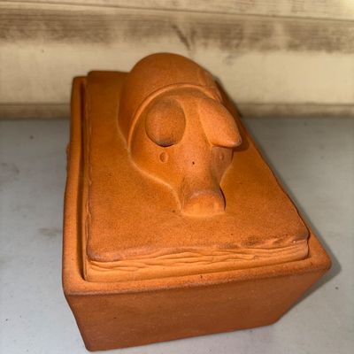 Sale Photo Thumbnail #354: A unglazed terracotta rectangular baking dish or terrine keeper featuring a lid molded with a sleeping pig motif. Shows light surface wear and minor discoloration consistent with use.
5X9in