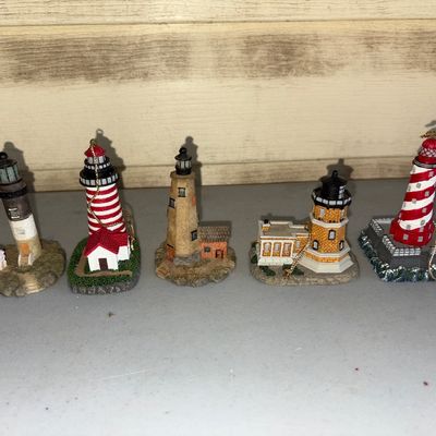 Sale Photo Thumbnail #137: A collection of five detailed miniature resin lighthouse figurines, including several with gold hanging cords to use as ornaments. Features various designs including red-and-white striped lighthouses, brick textures, and attached keeper's quarters. Appear