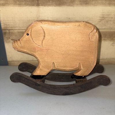 Sale Photo Thumbnail #302: Folk art style hand-carved wooden rocking pig figurine. Features carved ears, snout, and tail details with painted black hooves and eyes, mounted on dark wood rockers. Displays a crackle finish/patina on the body. Shows light age-appropriate wear.
6in tal