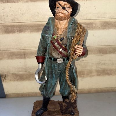 Sale Photo Thumbnail #232: A detailed cast resin pirate captain figurine featuring a hook hand, eye patch, tricorne hat with skull logo, coiled rope, and anchor detail resting on a faux wood base. Displays detailed paintwork and texture throughout. Good pre-owned condition with no 