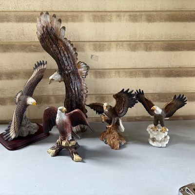 Sale Photo Thumbnail #56: A group of five resin and faux-wood/stone composition bald eagle statues in various soaring and perched poses. Includes one large eagle carving/figurine along with four smaller detailed eagle figurines on decorative display bases. Items appear to be in go