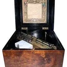 Antique Swiss cylinder music box housed in a wooden case with an ebonized interior lid featuring an ornate tune card, complete with a...