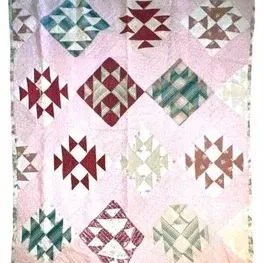 Handcrafted vintage quilt featuring geometric diamond-set star and arrowhead motifs against a soft pink background.