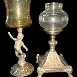 Pair of ornate vintage metal hurricane candle holders, featuring one with a cherub figural base and amber glass shade, and another with a...