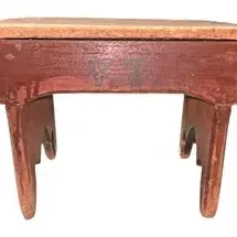 Vintage rustic wooden footstool featuring a reddish-brown painted finish and cut-out side legs, showing heavy distress and surface wear.