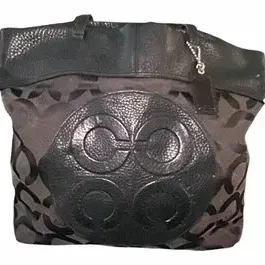 Coach black jacquard signature tote bag featuring a large pebbled leather front medallion and leather handles.