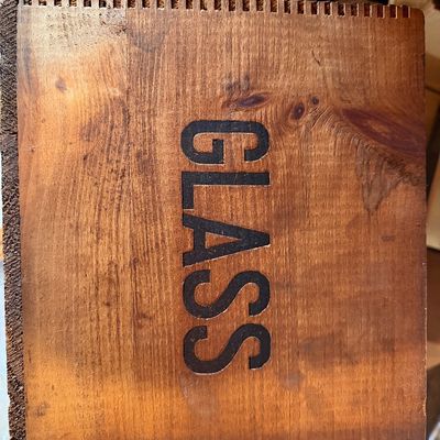 Vintage wooden crate or box lid with box-jointed edges, stenciled with the word GLASS in dark lettering.