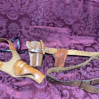 Sale Photo Thumbnail #55: Collection of vintage leather gun holsters, shoulder rigs, and cartridge belts, showing natural age and wear.