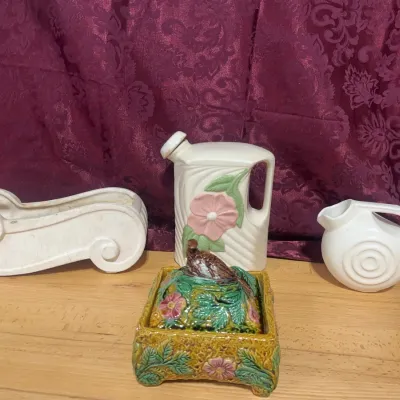 Sale Photo Thumbnail #137: Collection of vintage art pottery pieces, including a Hull Wildflower pitcher, a small majolica covered box with a bird finial, and two off-white decorative planters.