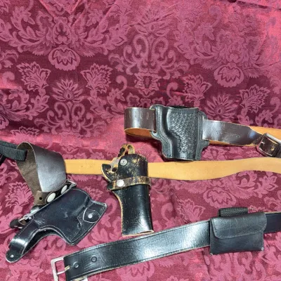 Sale Photo Thumbnail #56: Collection of vintage black and brown leather gun holsters, belts, and accessories showing varying degrees of wear.