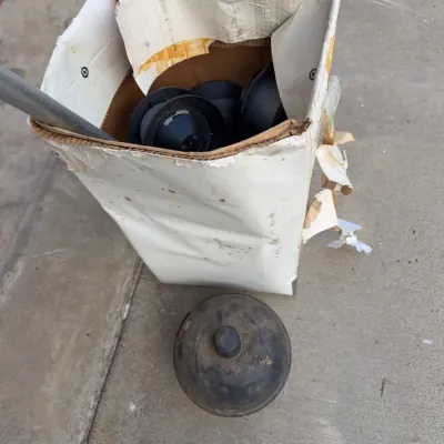 Sale Photo Thumbnail #254: Cardboard box filled with black rubber or plastic industrial components alongside a dusty round cap piece.