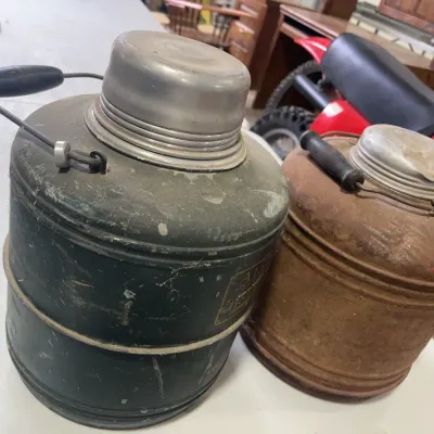 Sale Photo Thumbnail #156: Pair of vintage insulated picnic jugs featuring metal bodies with wooden bail handles, showing significant age-related wear and rust.