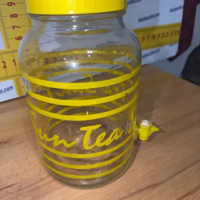 Sale Photo Thumbnail #200: Vintage glass Sun Tea jar beverage dispenser featuring bright yellow graphics, a yellow screw-on lid with flip top, and a plastic spigot.