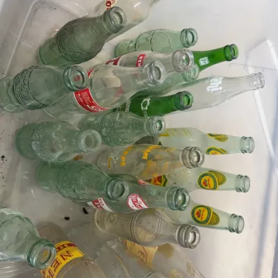 Sale Photo Thumbnail #250: Assorted collection of vintage glass soda bottles in a plastic bin, including Coca-Cola, Nehi, Sunkist, and Frostie brands.