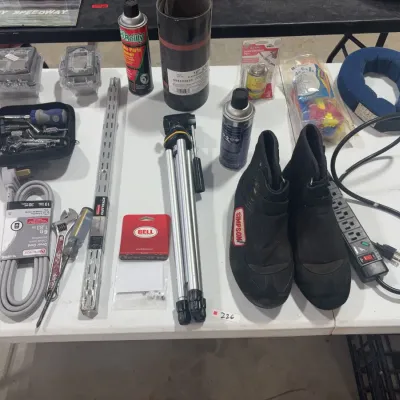 Sale Photo Thumbnail #87: Assortment of garage and racing supplies, including Simpson racing boots, a camera tripod, hand tools, spray cans, electrical cords, and hardware.