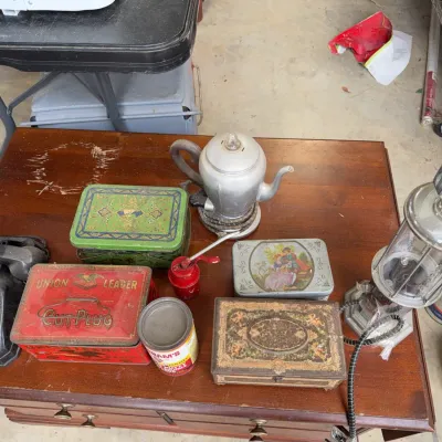 Sale Photo Thumbnail #251: Collection of vintage items including a black rotary telephone, metal coffee percolator, decorative tin boxes, small oil can, and a novelty gas pump table lamp on a wooden table.