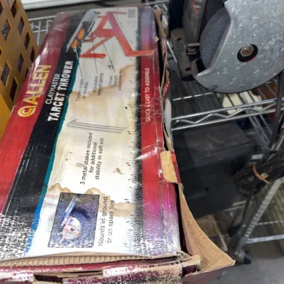 Sale Photo Thumbnail #218: Vintage Allen Claymaster Target Thrower in its original damaged box, sits next to an electric bench grinder.