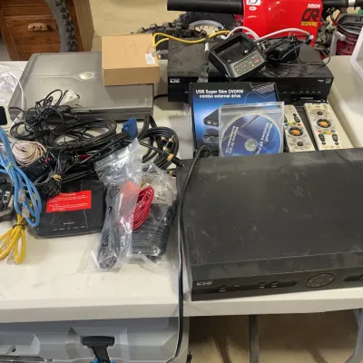 Sale Photo Thumbnail #158: Assortment of electronics including DirecTV receivers, a vintage Dell laptop, external DVD drive, security cameras, and various cables.