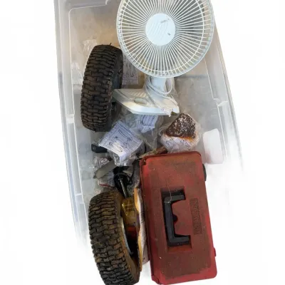 Sale Photo Thumbnail #106: Large clear plastic storage bin filled with miscellaneous household items including a white desk fan, small lawnmower tires, and a red plastic toolbox.