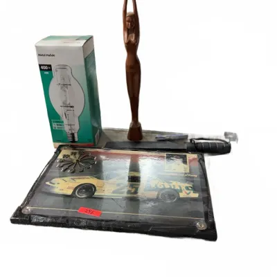 Sale Photo Thumbnail #114: Eclectic lot featuring a wooden stylized female figure sculpture, a framed Kodiak NASCAR race car wall clock, a fixed-blade knife in sheath, and a boxed 400W metal halide light bulb.