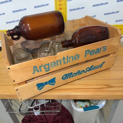 Sale Photo Thumbnail #201: Vintage Moño Azul Argentine Pears wooden crate filled with amber glass bottles, small mason jars, and an antique rusty metal ladle.