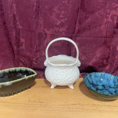 Sale Photo Thumbnail #126: Collection of mid-century art pottery pieces, including a white embossed footed basket planter, a dark green and beige drip-glaze dish, and a mottled blue glaze bowl.
