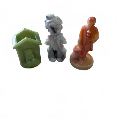 Sale Photo Thumbnail #298: Trio of vintage slag glass figurines, including a green doghouse match holder, a grey-and-white hobo figure, and an orange-and-pink colonial gentleman.