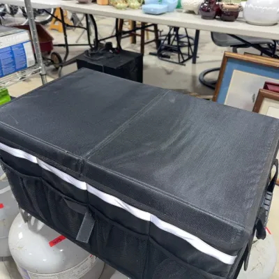 Sale Photo Thumbnail #184: Collapsible black fabric trunk and cargo organizer with side mesh pockets, shown resting on propane tanks in a sale venue.