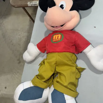 Sale Photo Thumbnail #187: Vintage plush Mickey Mouse doll wearing a red shirt with an 'M' logo, olive green cargo pants, and blue-and-white sneakers.