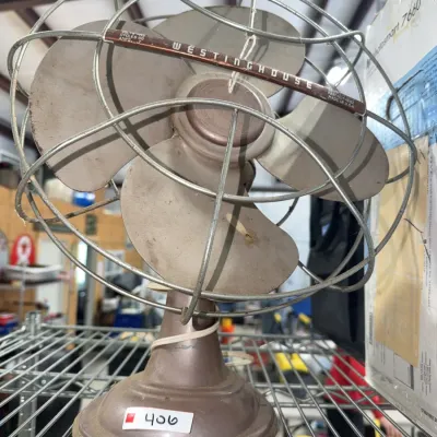 Sale Photo Thumbnail #182: Vintage Westinghouse metal electric desk fan featuring a four-blade design and protective wire cage.