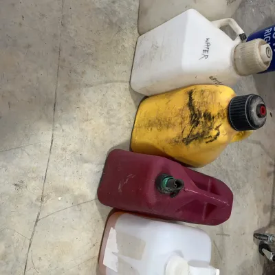 Sale Photo Thumbnail #32: Assorted plastic utility jugs and fuel cans lined up on a concrete floor, showing signs of heavy use and handwritten labels.