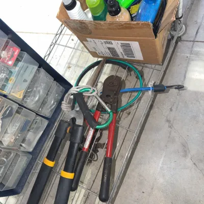 Sale Photo Thumbnail #210: Assorted yard and hand tools, including loppers and bolt cutters, resting on a wire shelf alongside a box of cleaning spray bottles.