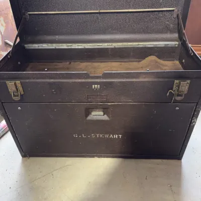 Sale Photo Thumbnail #235: Vintage dark brown metal machinist toolbox featuring a combination lock, metal latches, and stenciled name 'G. L. STEWART' on the front.