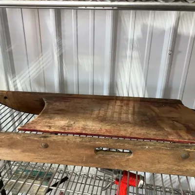 Sale Photo Thumbnail #27: Vintage wooden sled featuring a distressed patina, worn red trim on the seat, and hand-cut wooden runners, displayed on a wire storage rack.