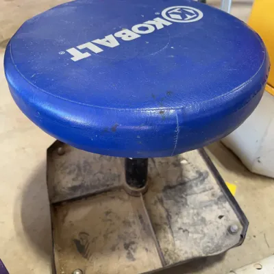 Sale Photo Thumbnail #43: Kobalt rolling mechanic's stool featuring a blue cushioned seat and a built-in metal tool tray base, showing minor wear from workshop use.