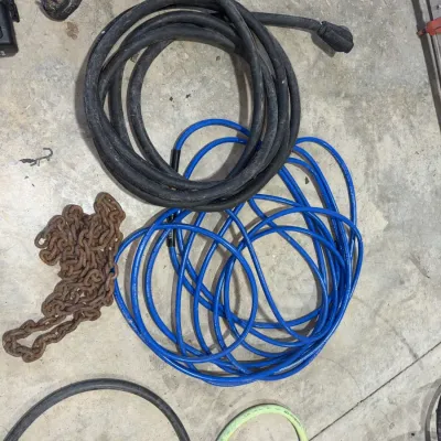 Sale Photo Thumbnail #92: Heavy-duty black generator extension cord, blue air compressor hose, and a length of rusted metal chain on a concrete floor.