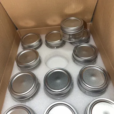 Sale Photo Thumbnail #207: Cardboard box containing a set of small glass canning jars with silver screw-top lids, arranged in custom foam packaging.