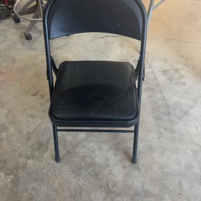 Sale Photo Thumbnail #79: Black metal folding chair featuring a padded vinyl seat and backrest, showing light wear.