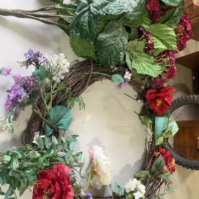 Sale Photo Thumbnail #160: Large circular grapevine wreath decorated with colorful artificial flowers alongside extra faux foliage branches.